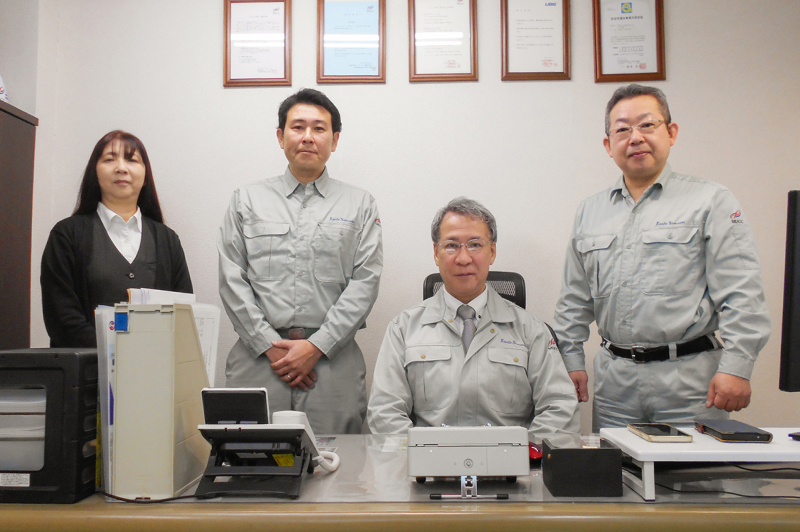 画像：オフィスに並ぶ作業着の男性と女性事務員